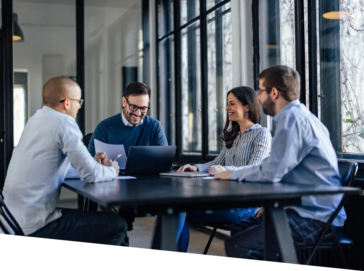 three people sitting at a table with a laptop and papers